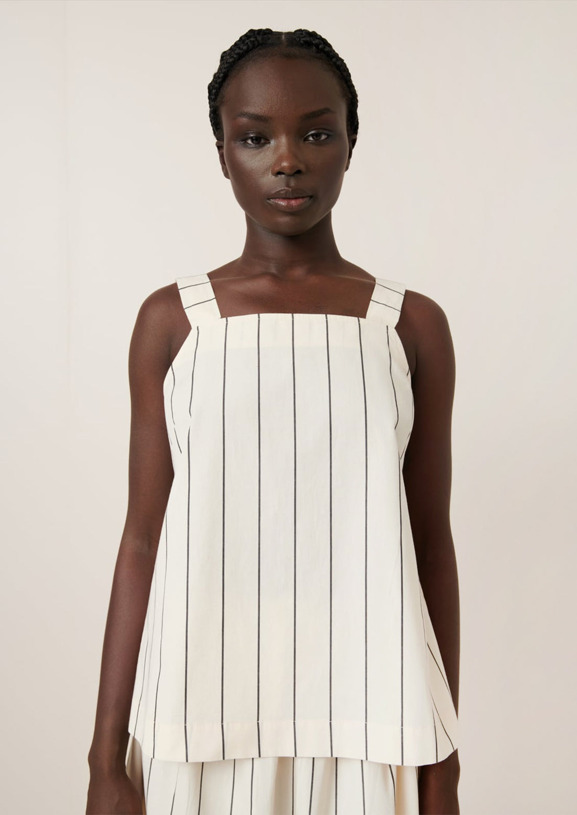 A person wearing a sleeveless top with square neckline, in cream with black pinstripe.