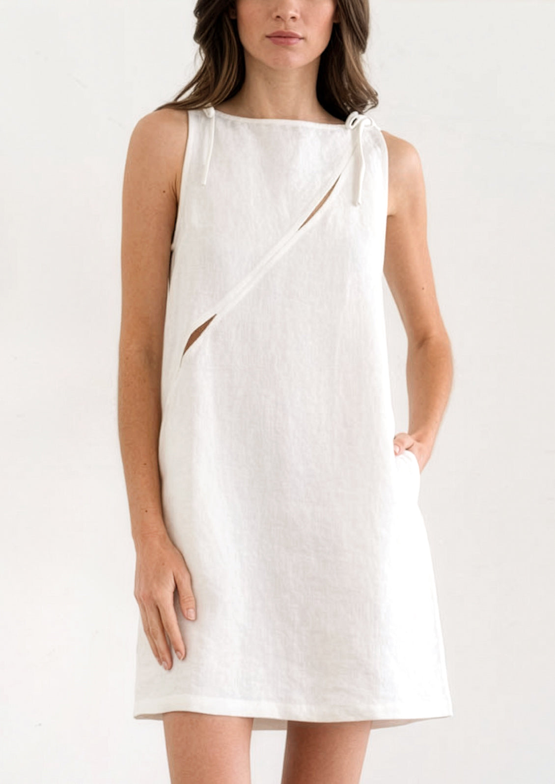A person wearing an A-line mini dress in white with diagonal slit detail across chest.