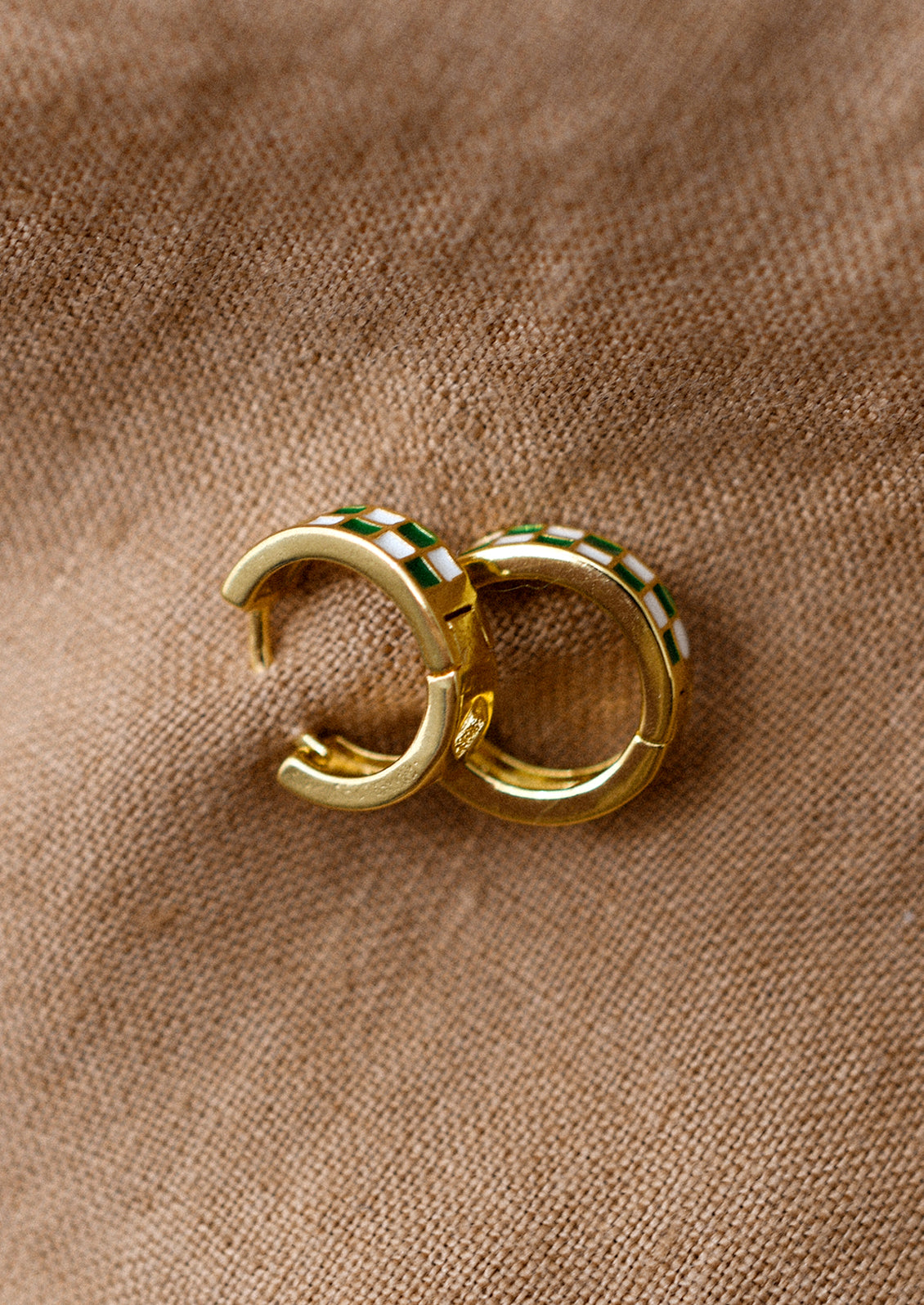 A pair of gold hoop earrings with green and white enamel checker pattern.