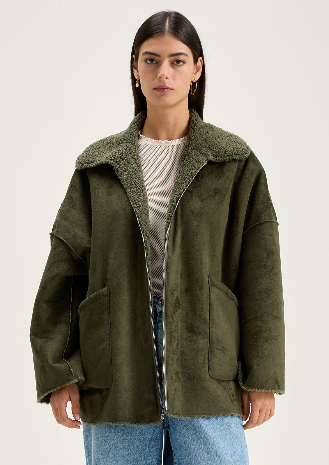 A woman wearing a reversible olive green jacket with suede side and shearling side.