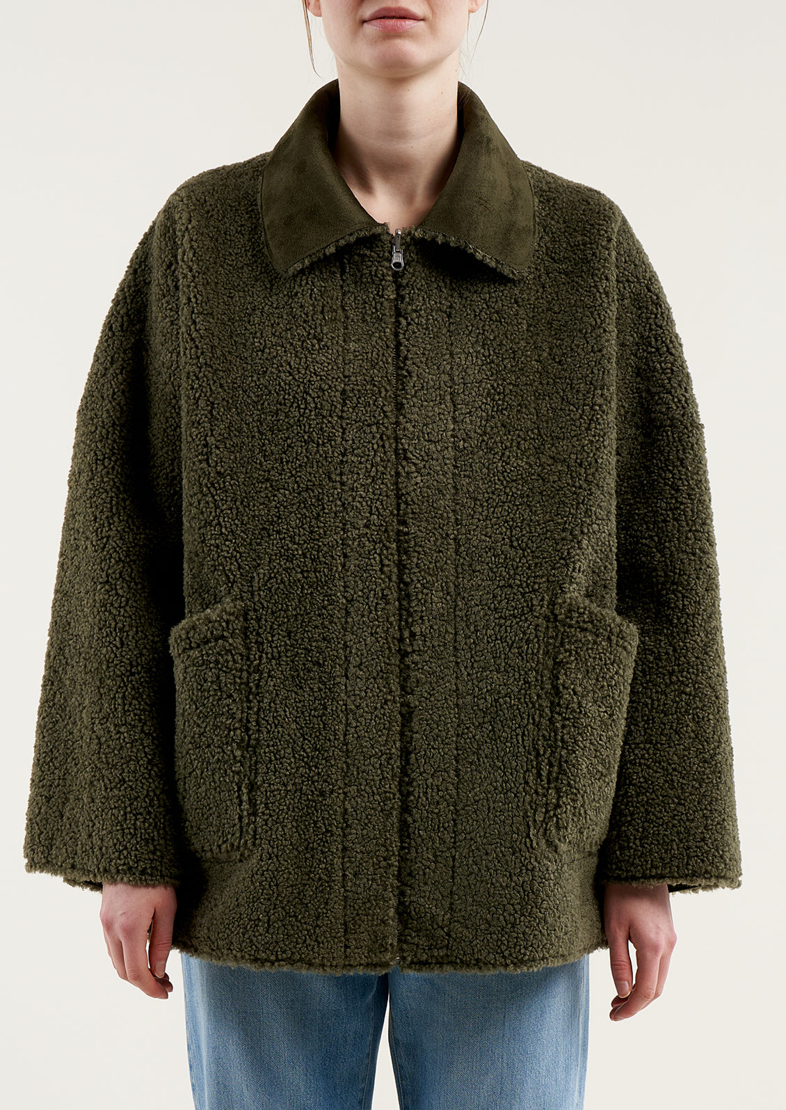 A woman wearing a reversible olive green jacket with suede side and shearling side.