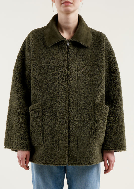 A woman wearing a reversible olive green jacket with suede side and shearling side.