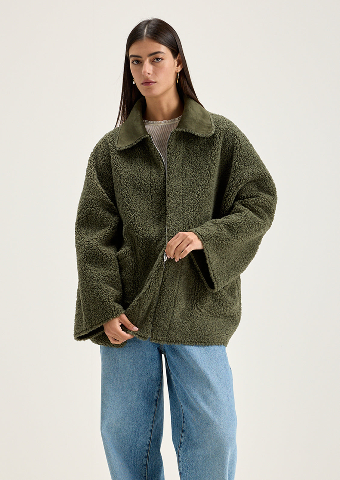A woman wearing a reversible olive green jacket with suede side and shearling side.