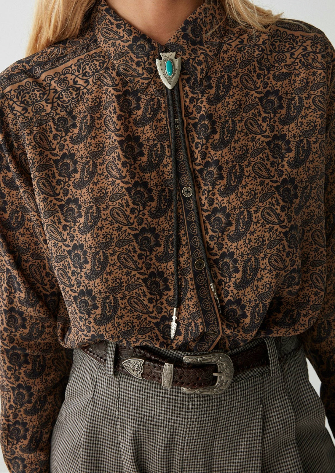 A woman wearing a paisley print blouse in brown and black.