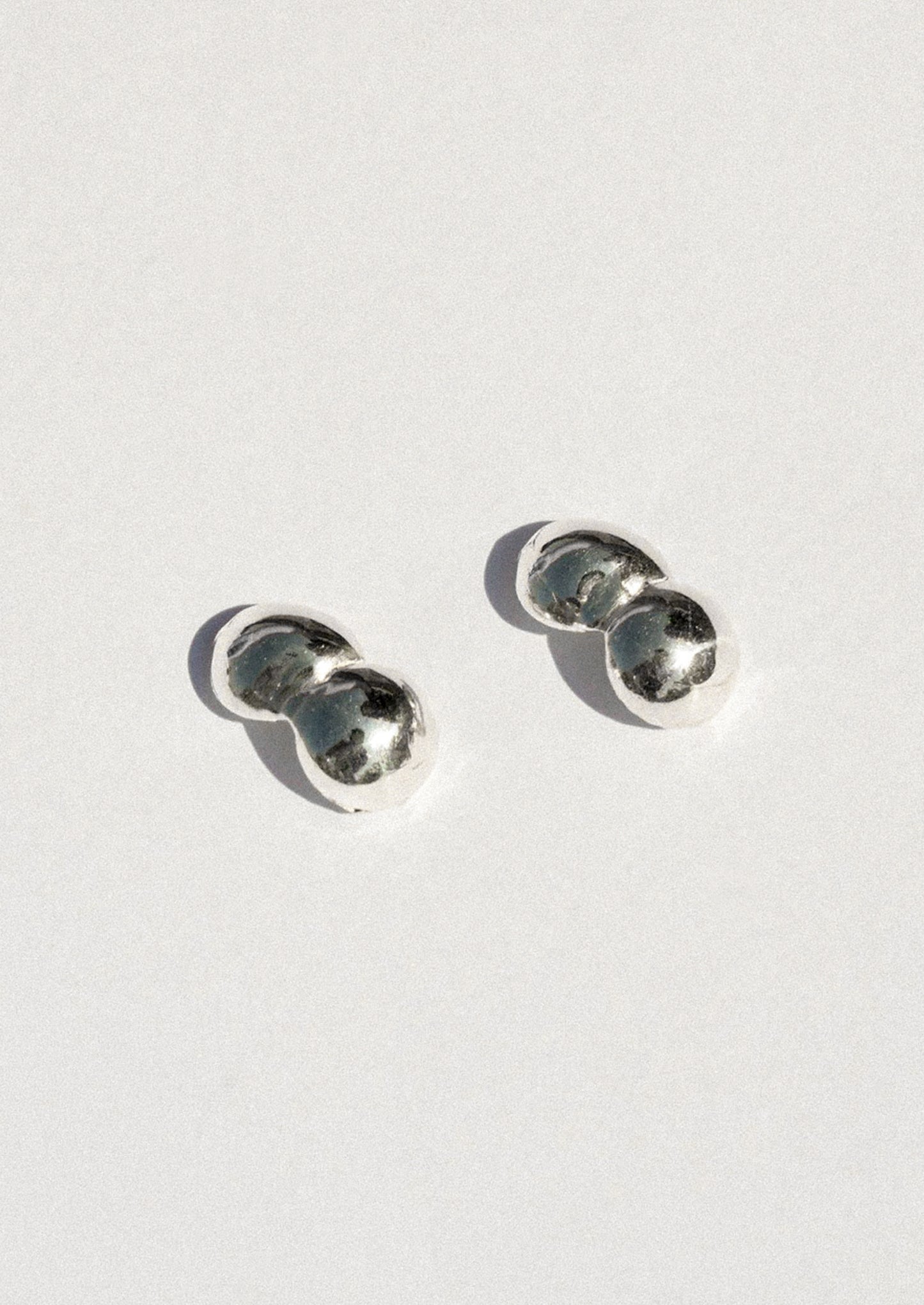 A pair of small silver stud earrings with a double-bubble design, photographed on a clean white background with soft shadows.