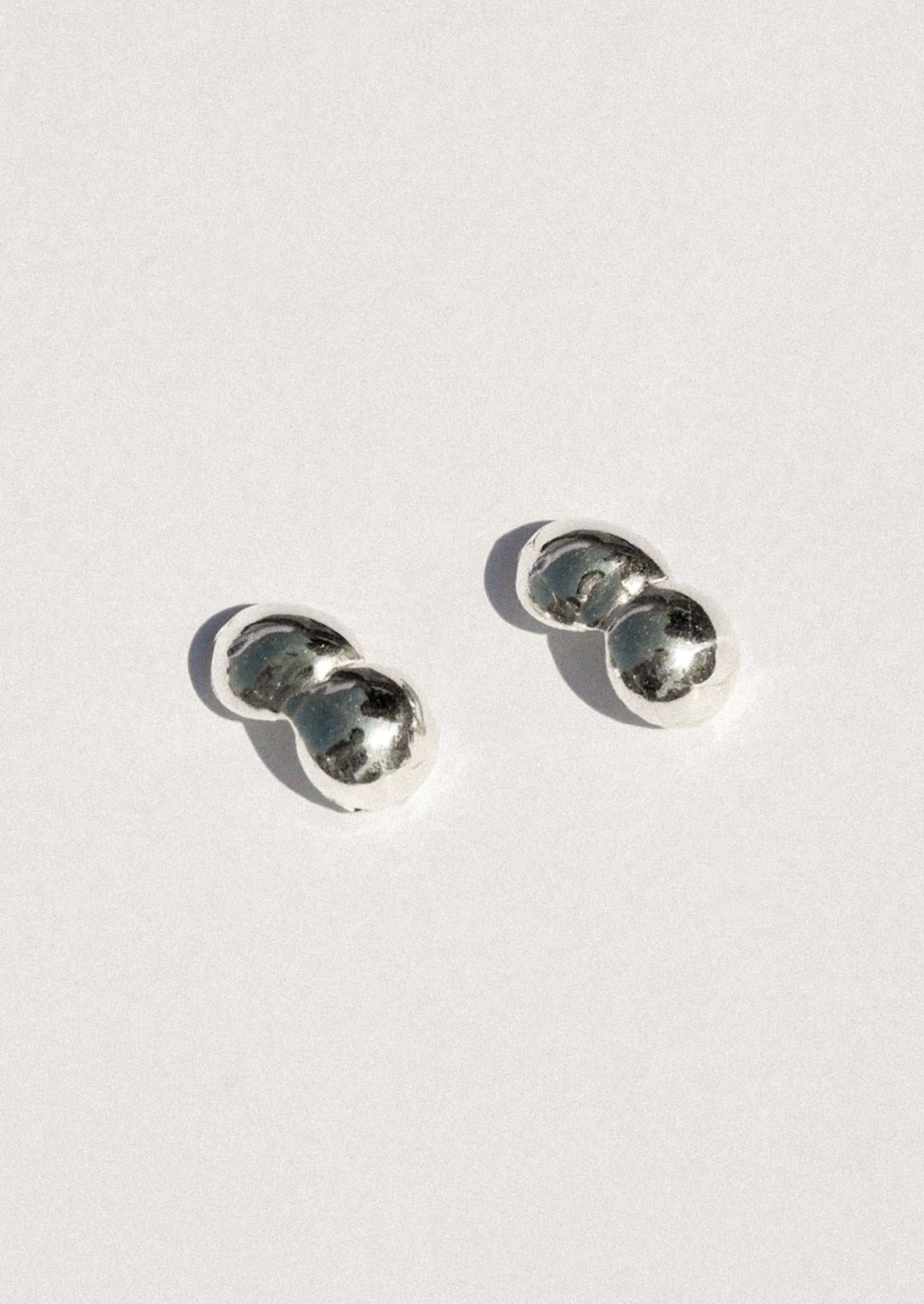 A pair of small silver stud earrings with a double-bubble design, photographed on a clean white background with soft shadows.