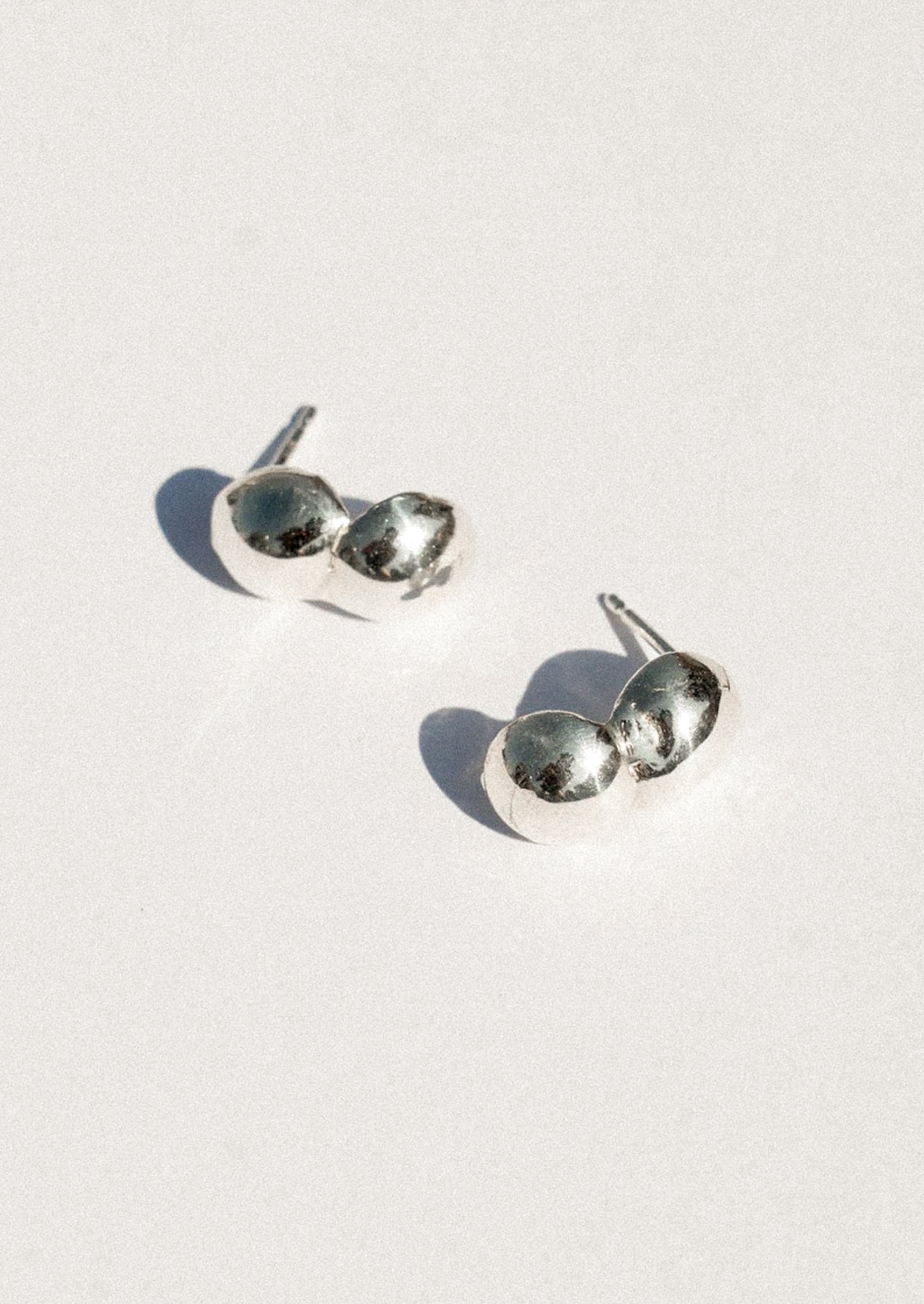 A pair of silver stud earrings with a unique double-oval design, photographed on a clean white background with soft shadows.