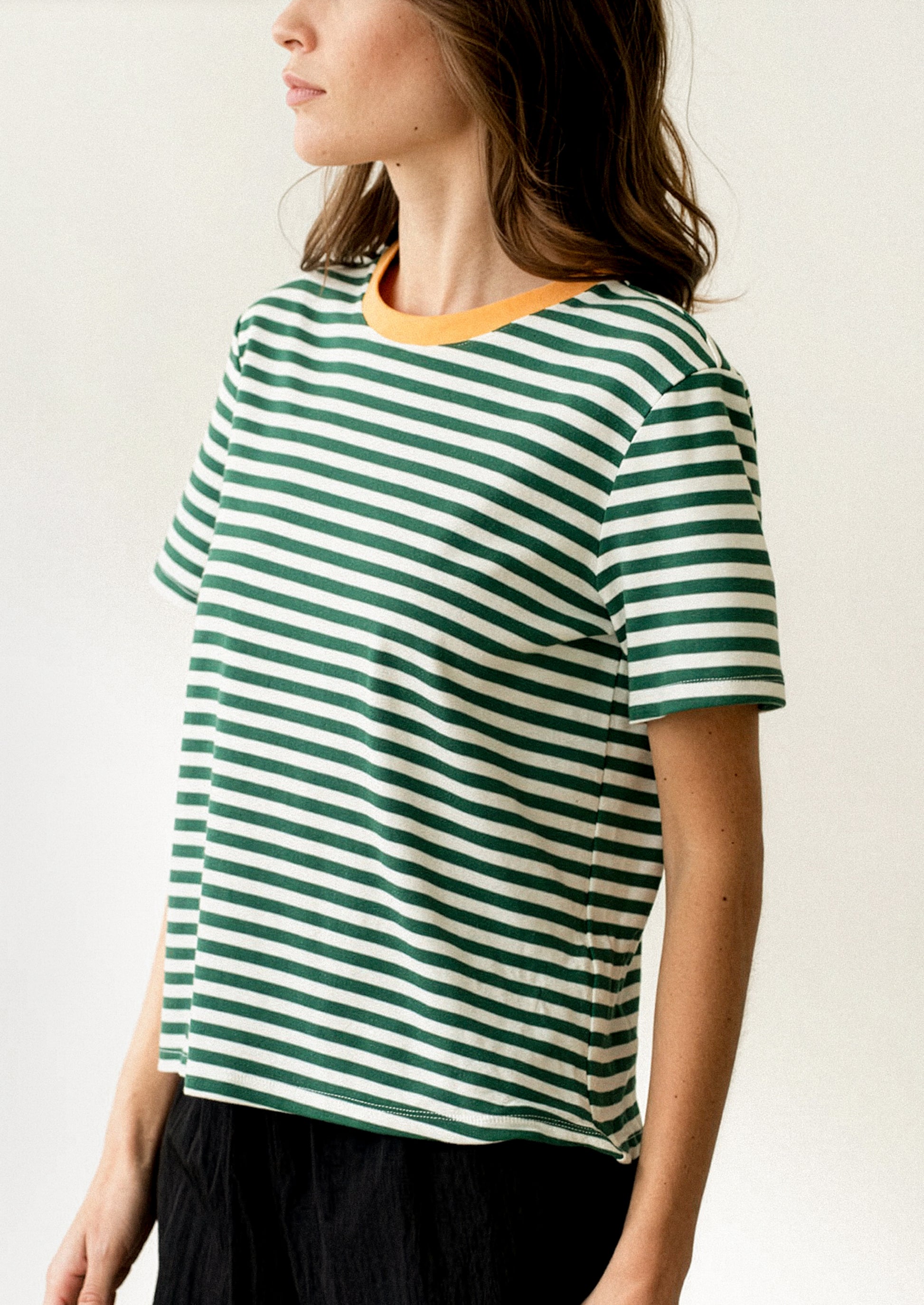 A woman wearing a short sleeve t-shirt in green and white stripes with orange neck trim.