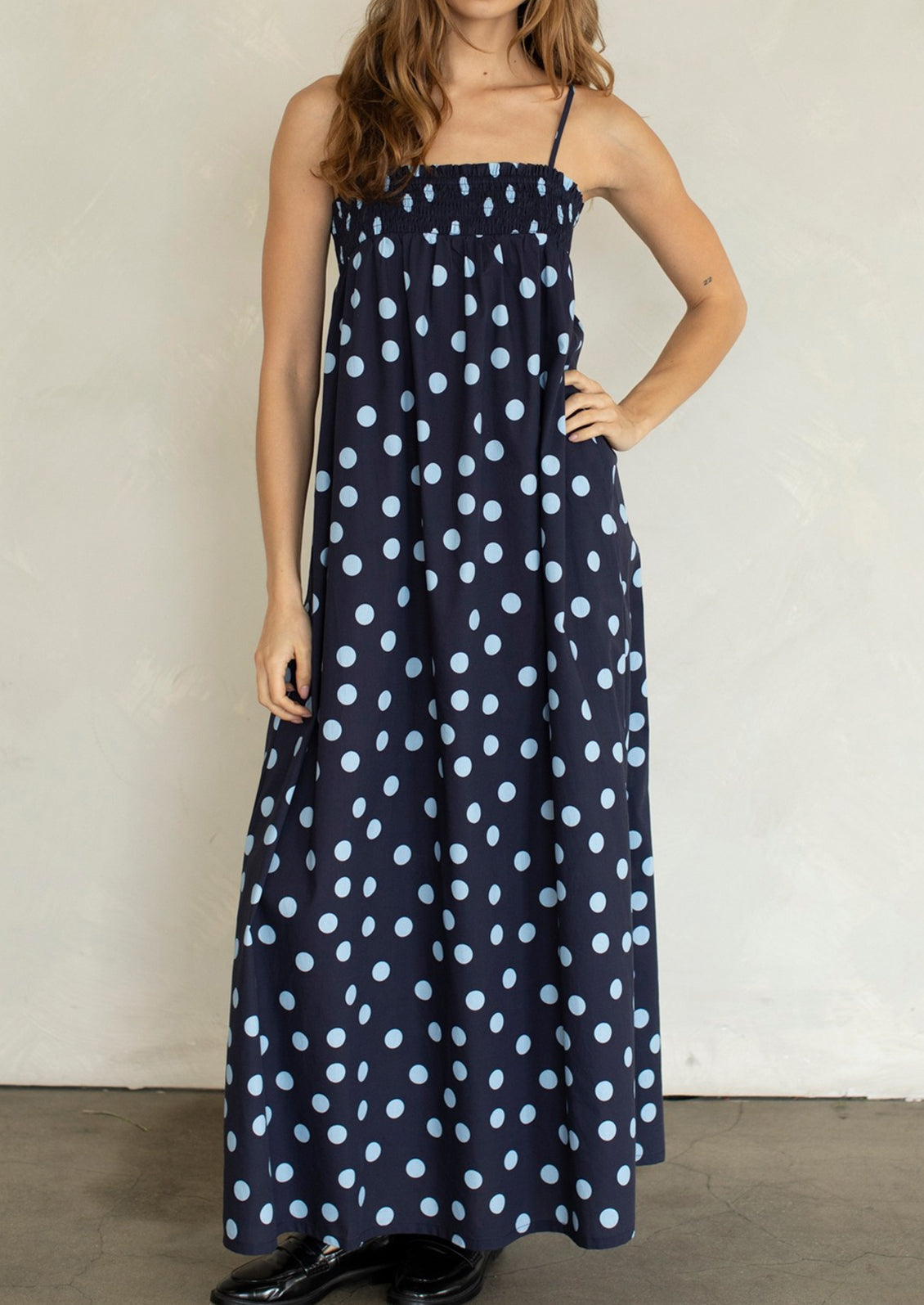 Woman wearing a navy blue dress with white polka dots against a plain background