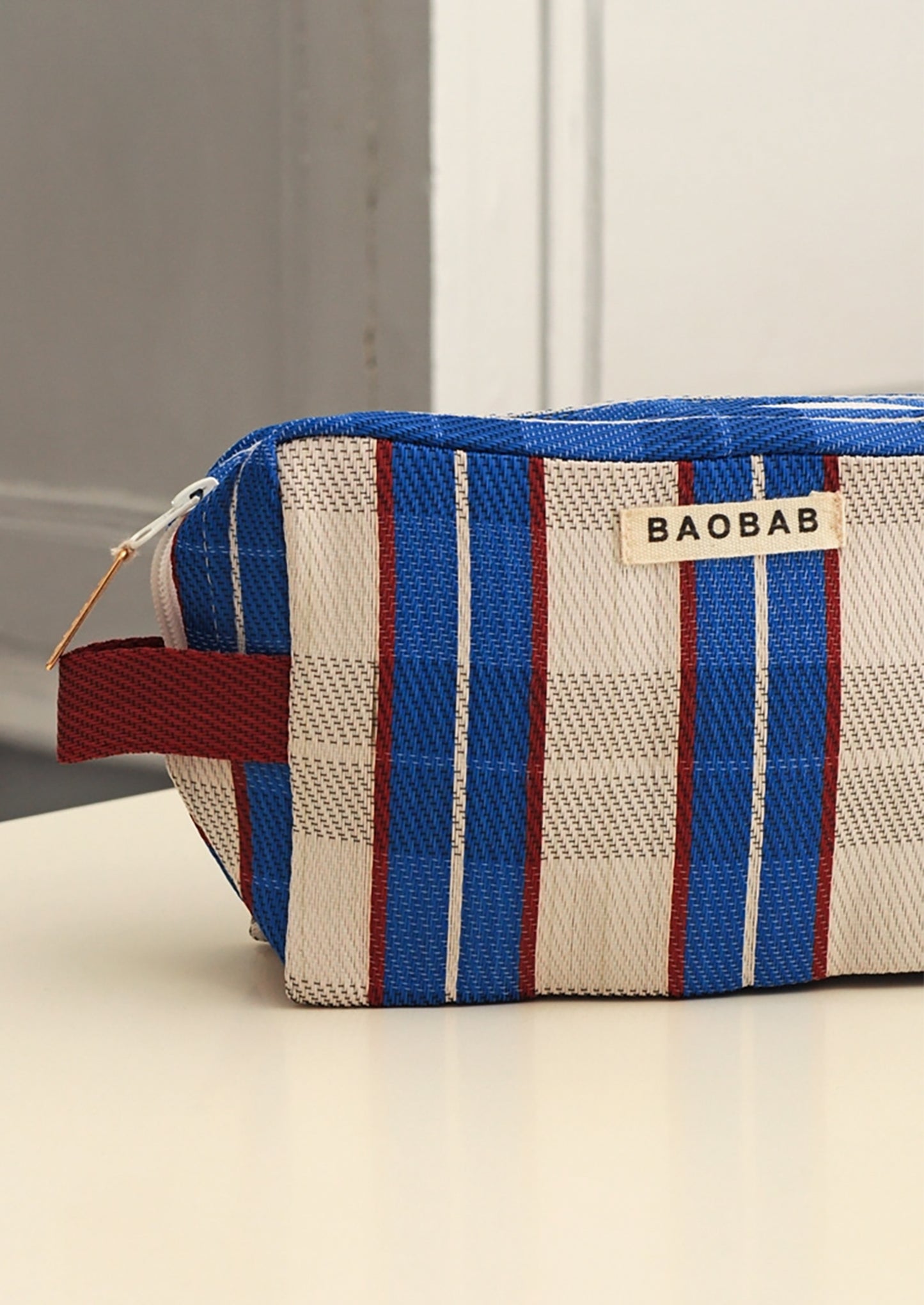 A BAOBAB brand zippered cosmetic pouch with a blue, white, and red plaid pattern, resting on a light-colored surface.