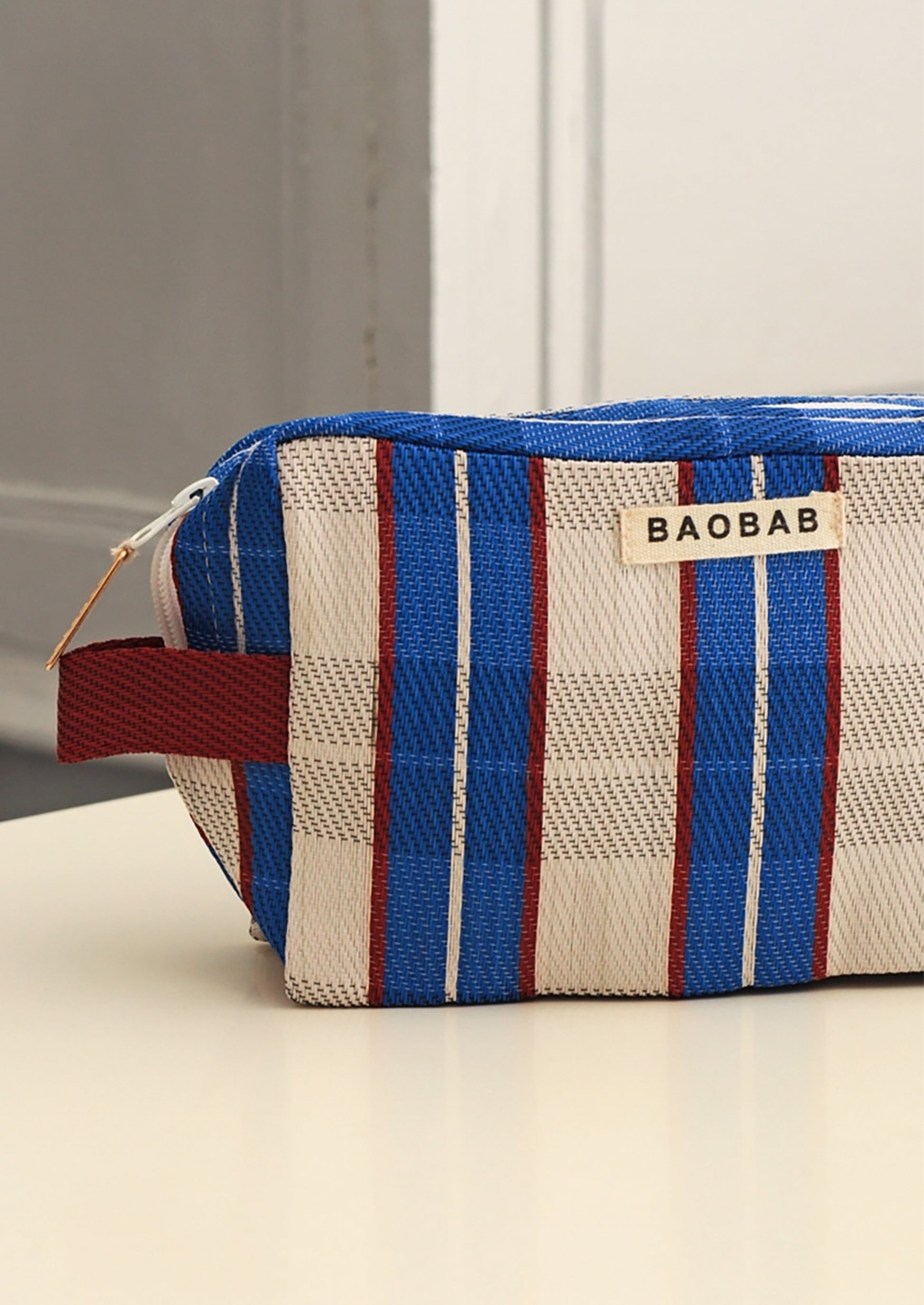 A BAOBAB brand zippered cosmetic pouch with a blue, white, and red plaid pattern, resting on a light-colored surface.