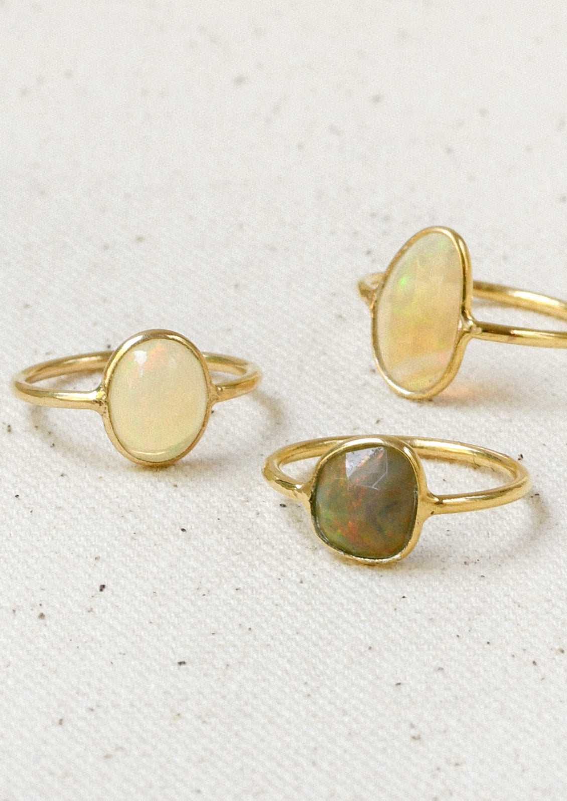 Three gold rings each with a natural Ethiopian opal bezeled in the center in varying sizes and colors.