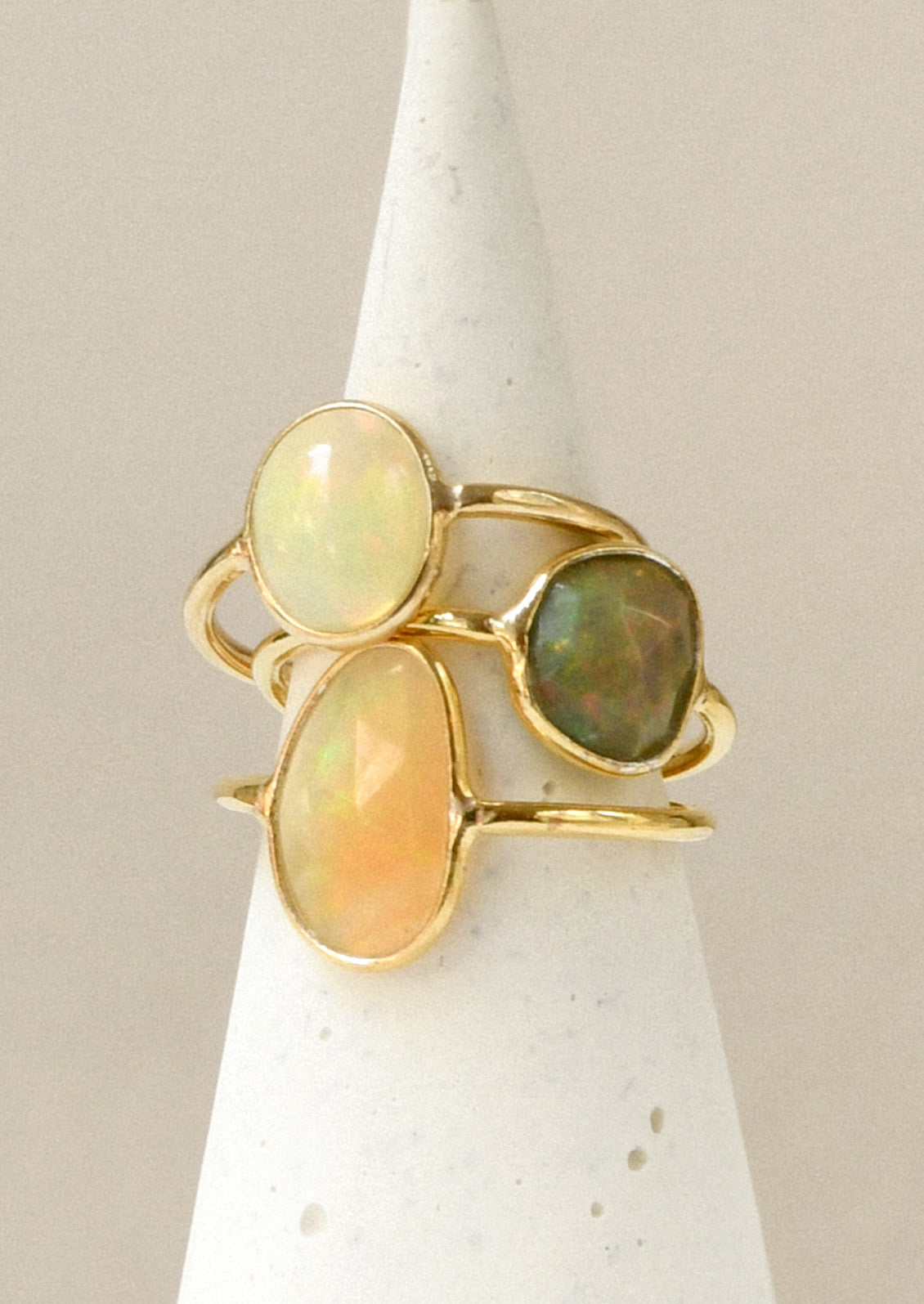 A stack of three gold rings each with a natural Ethiopian opal bezeled in the center in varying sizes and colors.