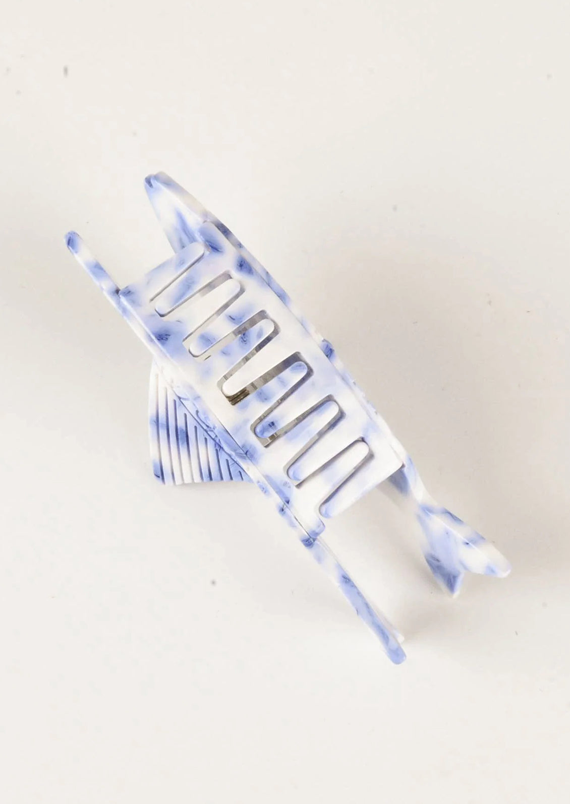 A blue and white hair claw in the shape of fish with carved floral pattern.