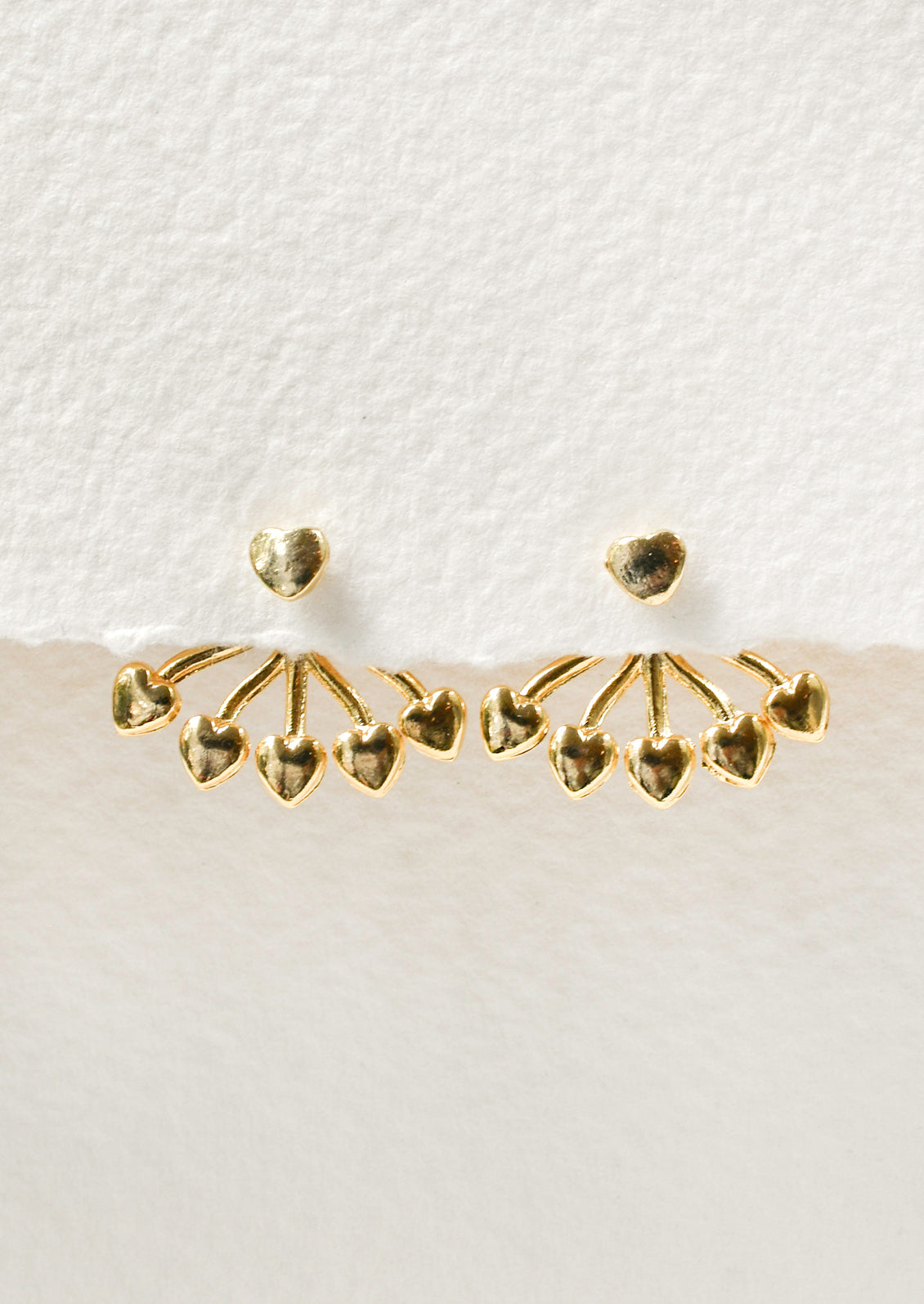 A pair of gold earrings with a heart shaped stud and five small hearts hanging below that attach on the back of the ear. 