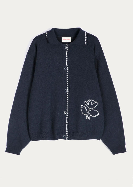 A dark navy blue knit cardigan sweater with white embroidered details, including a rose motif on the lower right side and decorative trim along the collar and front button placket, shown against a light off-white background.