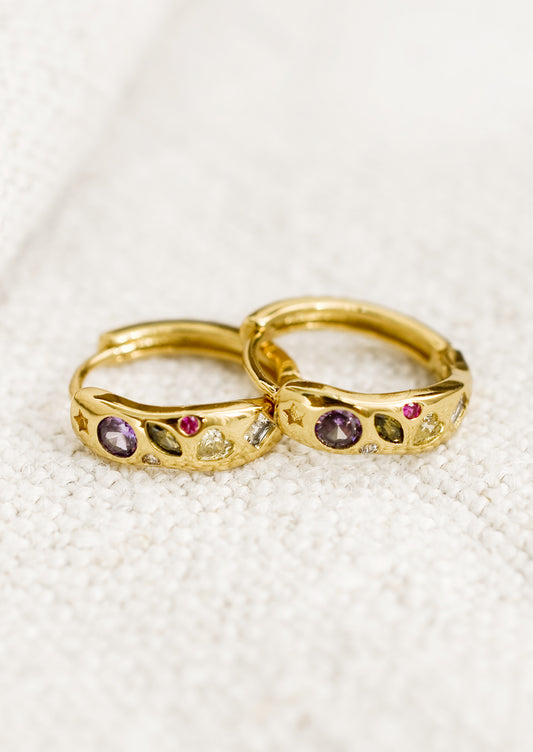 A pair of gold huggie hoops with embedded crystals in a mix of colors and shapes.