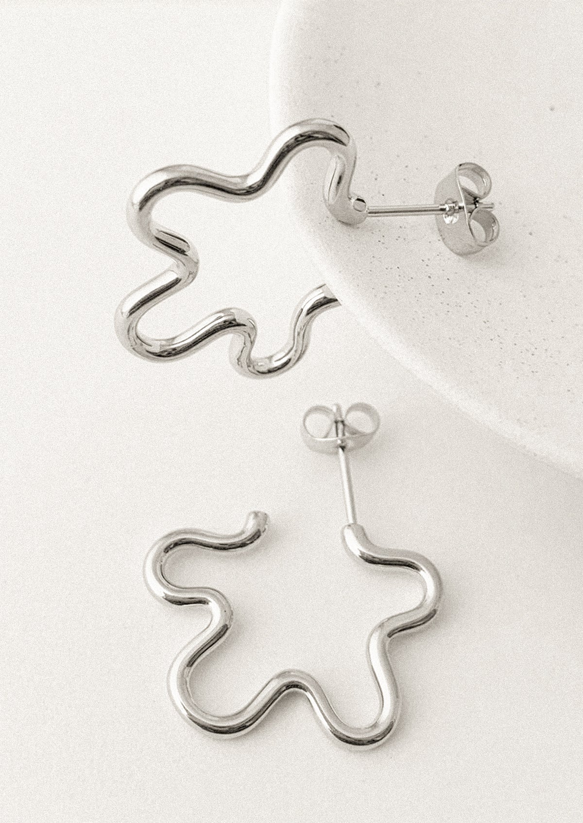 A pair of silver wavy hoop-style stud earrings with butterfly backings, displayed on a clean white surface.