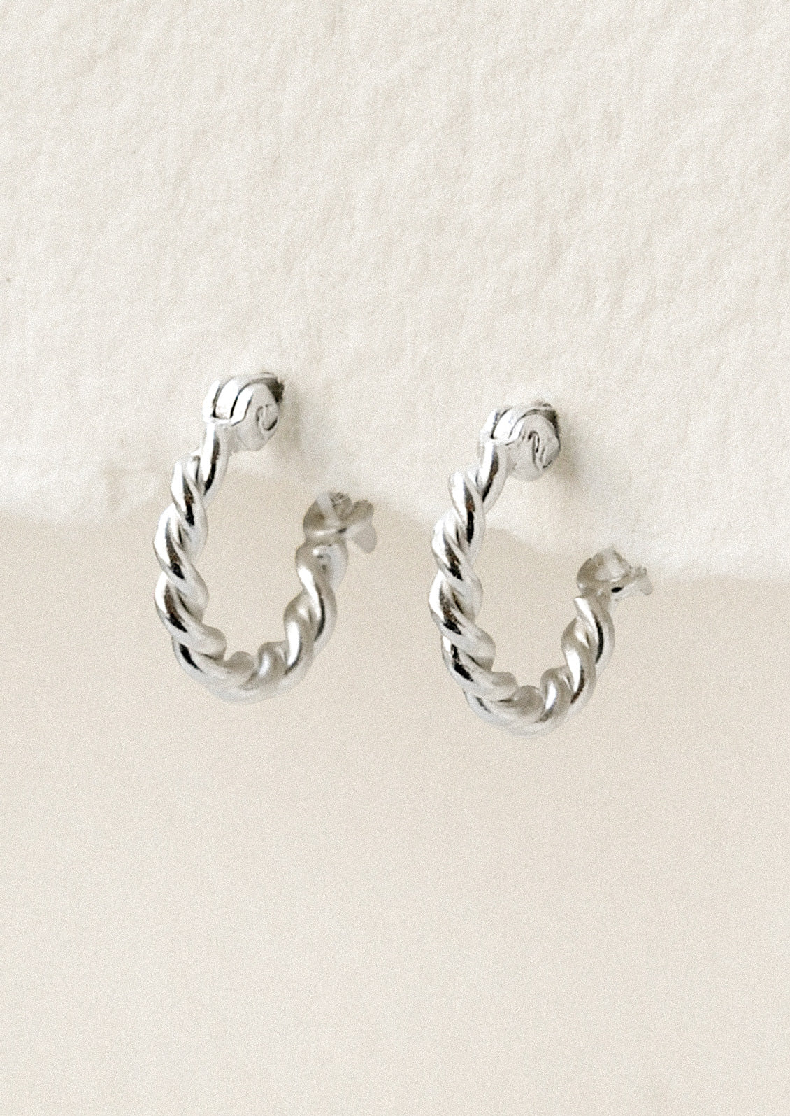 A pair of small silver hoop earrings with a twisted design.