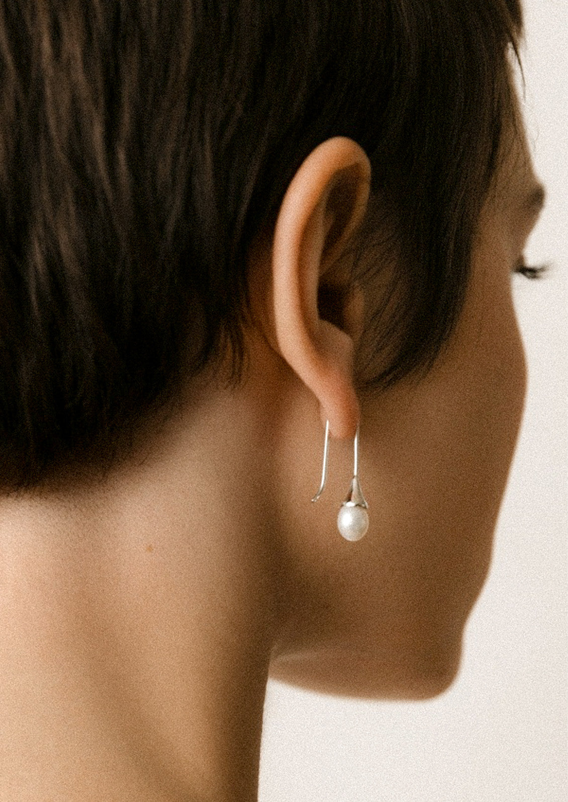 A woman wearing a sterling silver dangling earring with a freshwater pearl at the end.