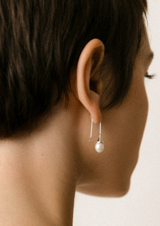 A woman wearing a sterling silver dangling earring with a freshwater pearl at the end.