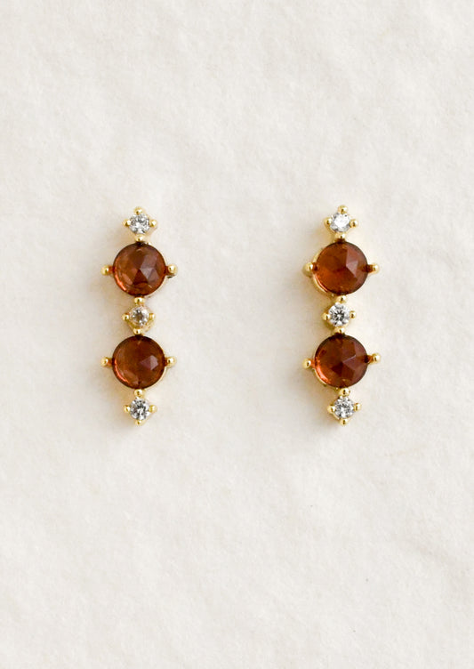 A pair of stud earrings with two garnet stones between smaller cubic zirconia stones.