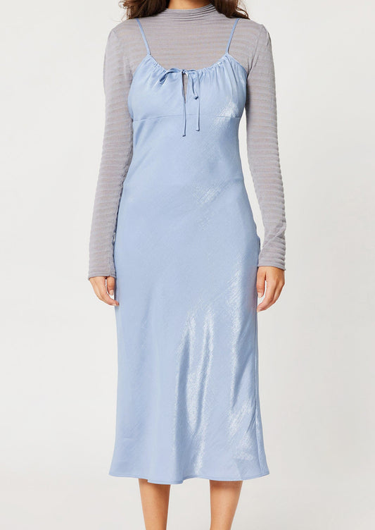 A woman wearing a periwinkle color sleeveless satin dress with empire silhouette.