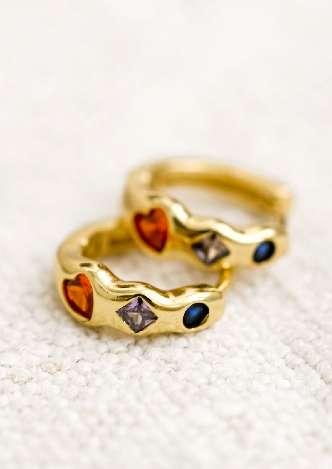 A pair of gold huggie hoop earrings with multicolor and multishape crystal detailing.