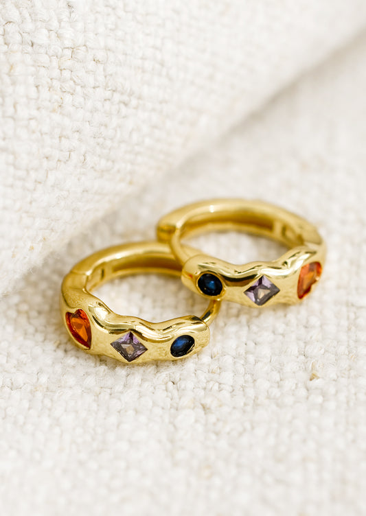 A pair of gold huggie hoop earrings with multicolor and multishape crystal detailing.