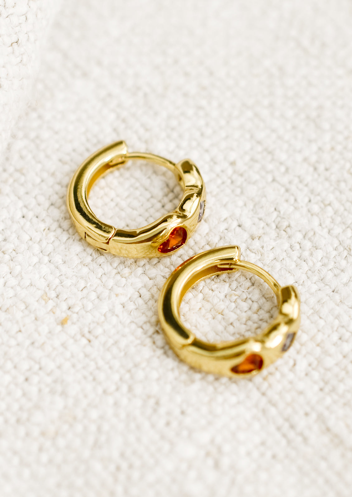 A pair of gold huggie hoop earrings with multicolor and multishape crystal detailing.