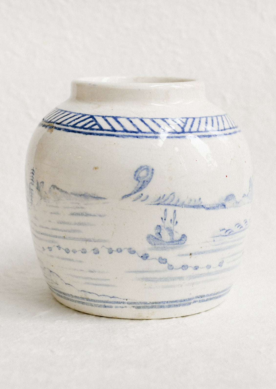An antique white ginger jar with faded blue painted scene.