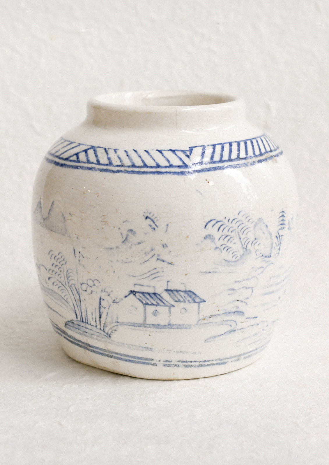An antique white ginger jar with faded blue painted scene.