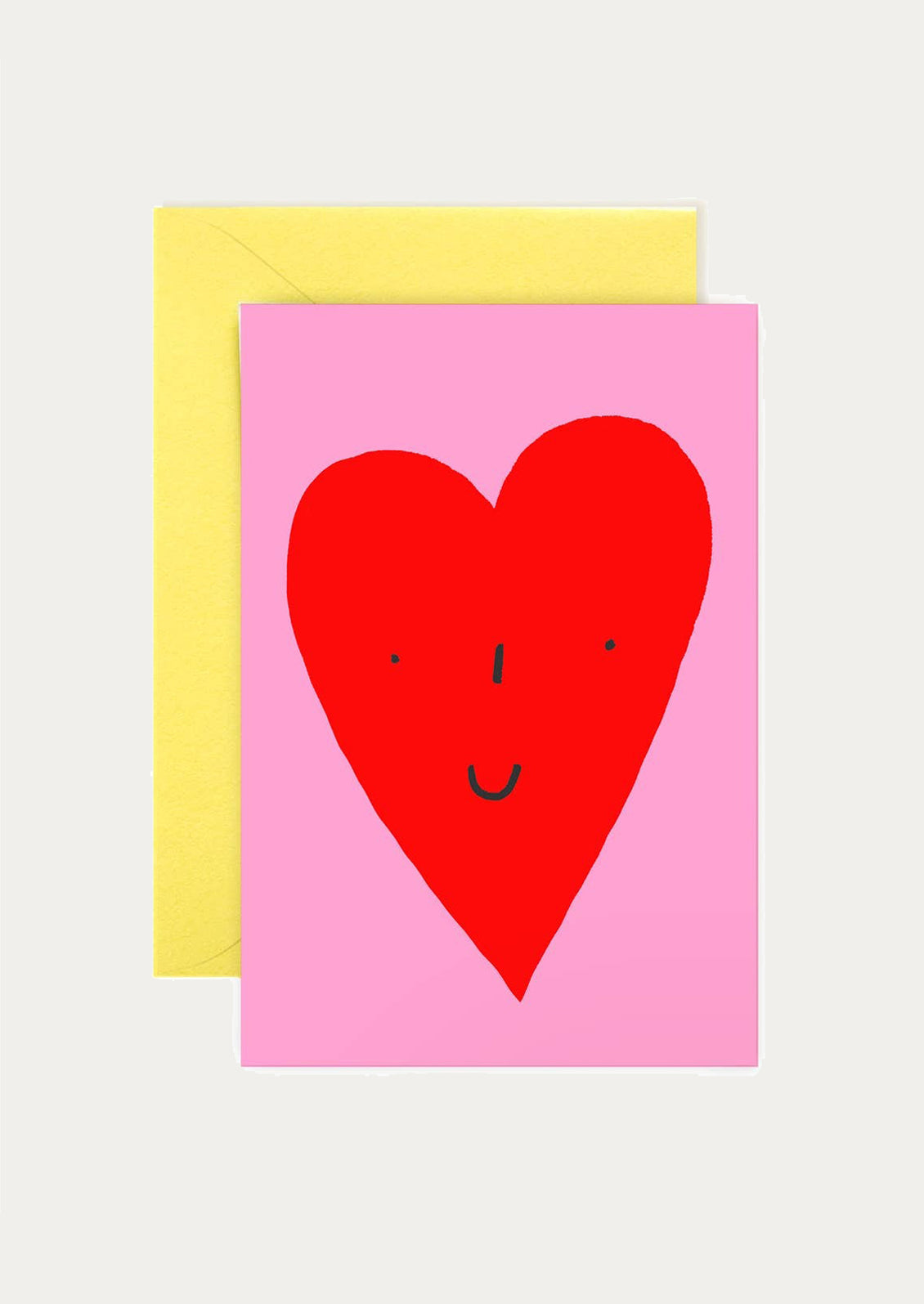 Card with a red heart face on a pink background, yellow envelope behind