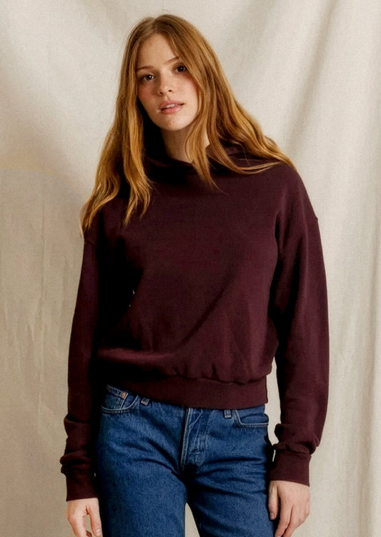 A person wearing a long sleeve hooded sweatshirt in burgundy color.