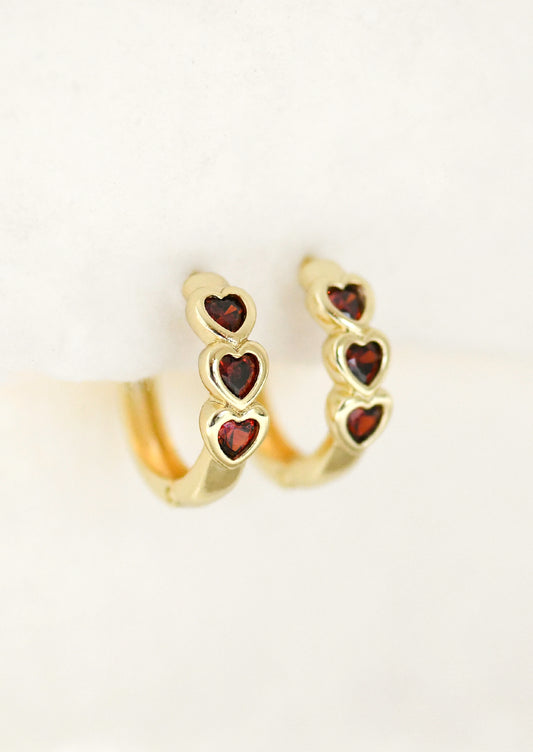 A pair of gold hoop earrings with three ruby red hearts.
