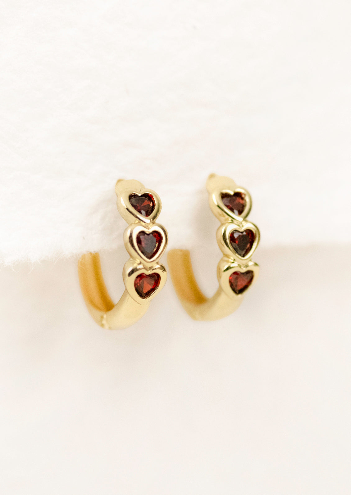 A pair of gold hoop earrings with three ruby red hearts.
