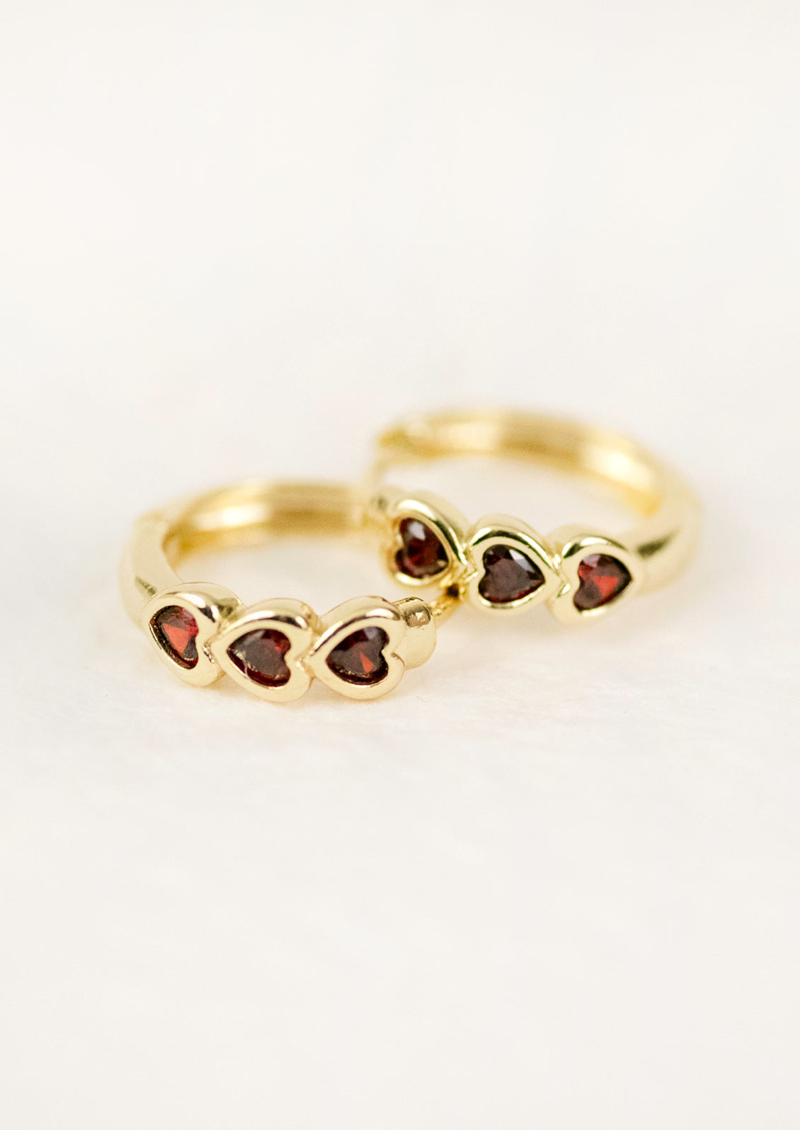 A pair of gold hoop earrings with three ruby red hearts.