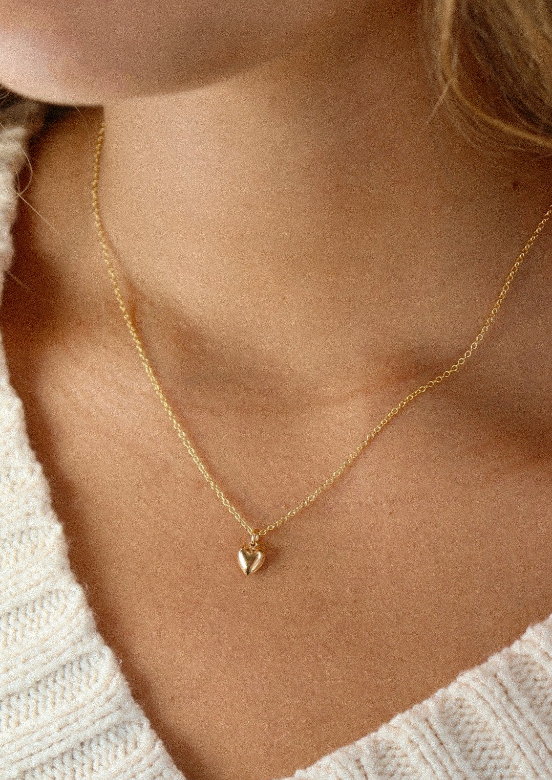 A gold necklace with a small heart charm.