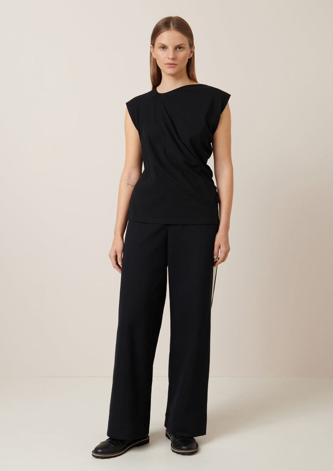 A woman wearing a black cap sleeve t-shirt with drape front detail.