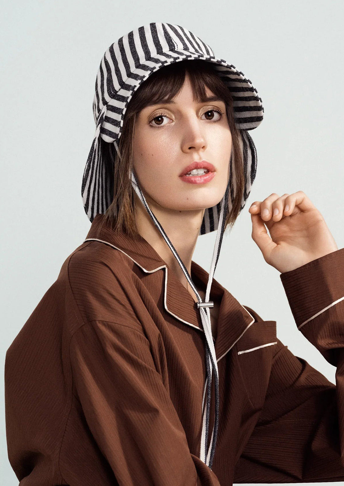Woman wearing a brown outfit and striped hat against a light background