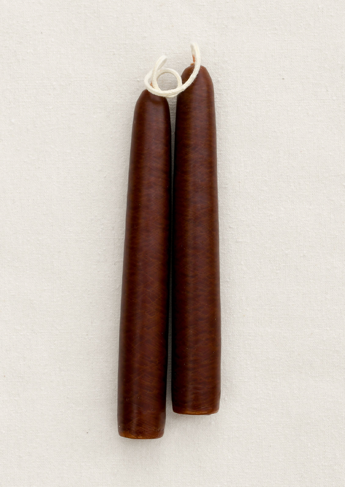 A pair of short brown taper candles on a brown background.