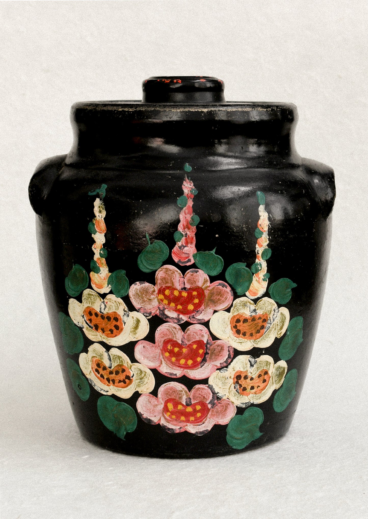 A vintage lidded crock in black with hand painted hollyhock pattern in pink and yellow.