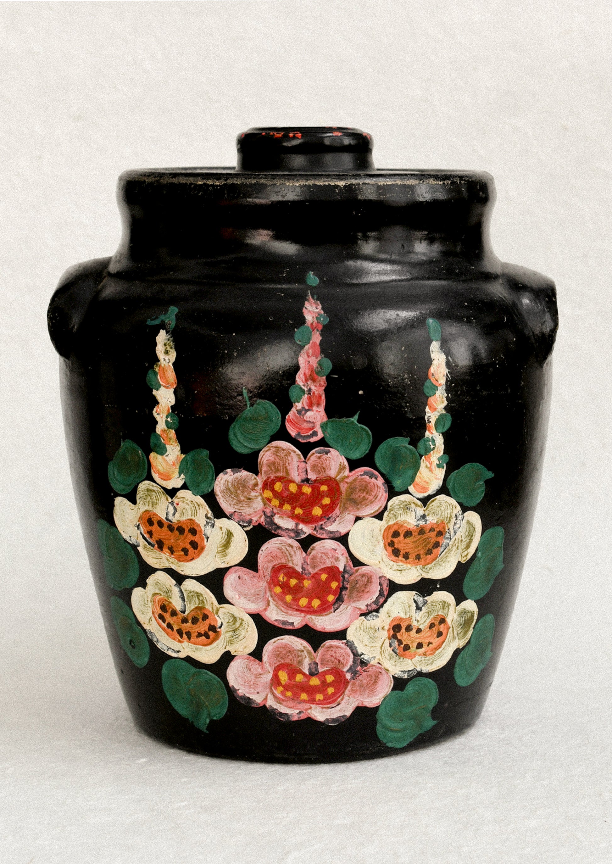 A vintage lidded crock in black with hand painted hollyhock pattern in pink and yellow.