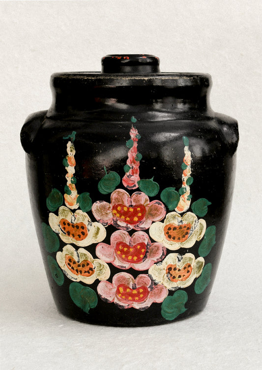A vintage lidded crock in black with hand painted hollyhock pattern in pink and yellow.