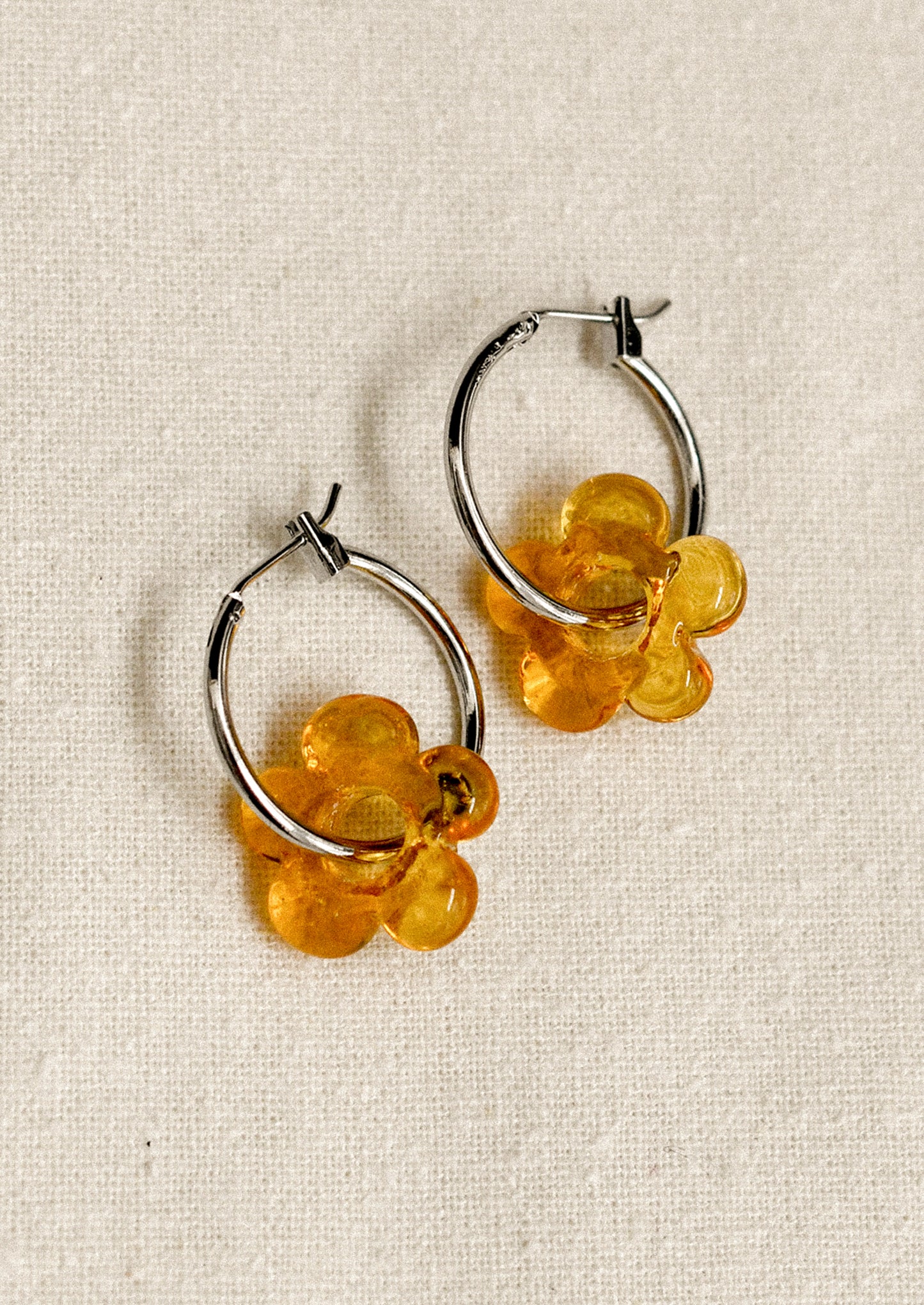 Pair of hoop earrings with amber floral charms on a beige fabric background