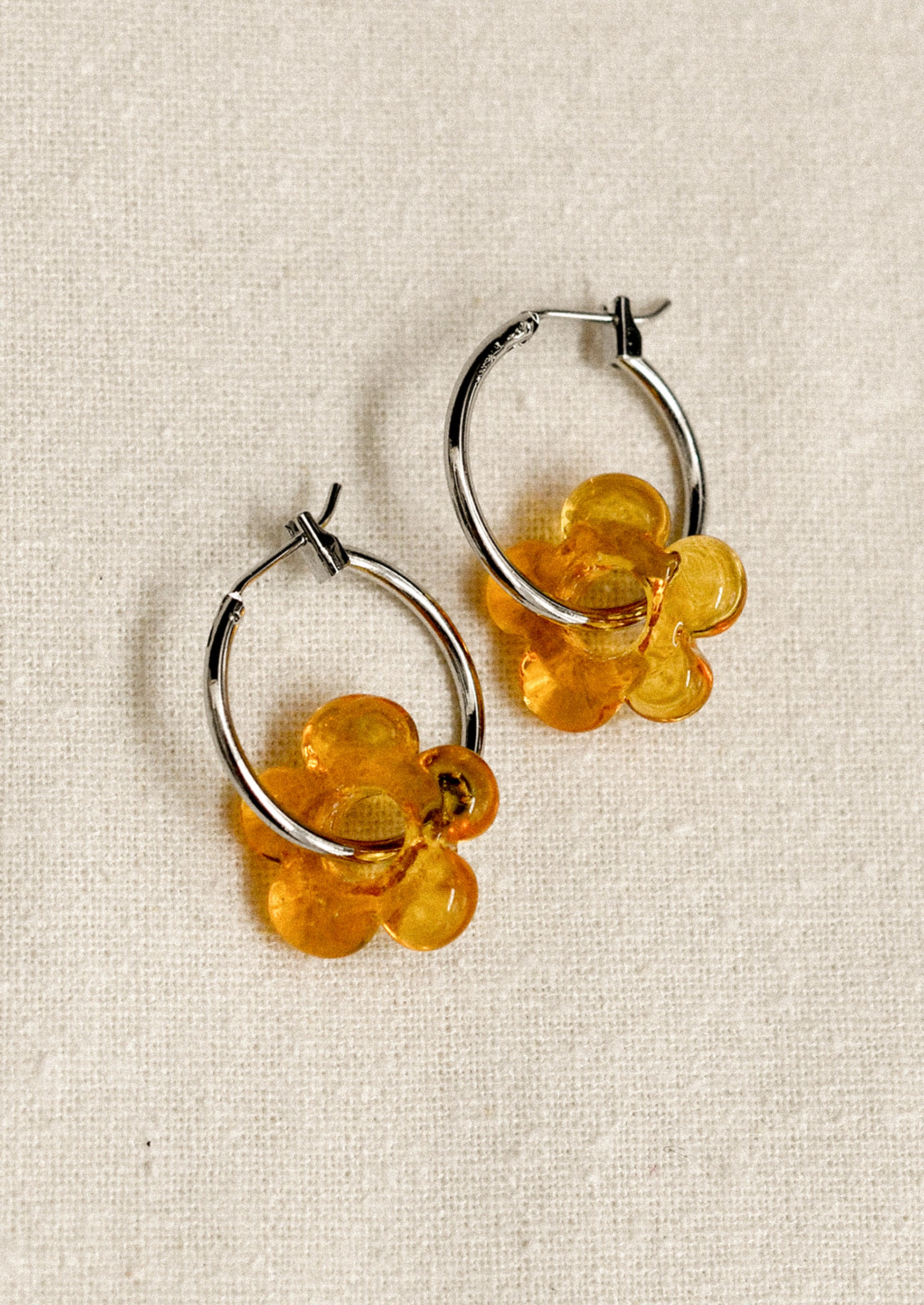 Pair of hoop earrings with amber floral charms on a beige fabric background