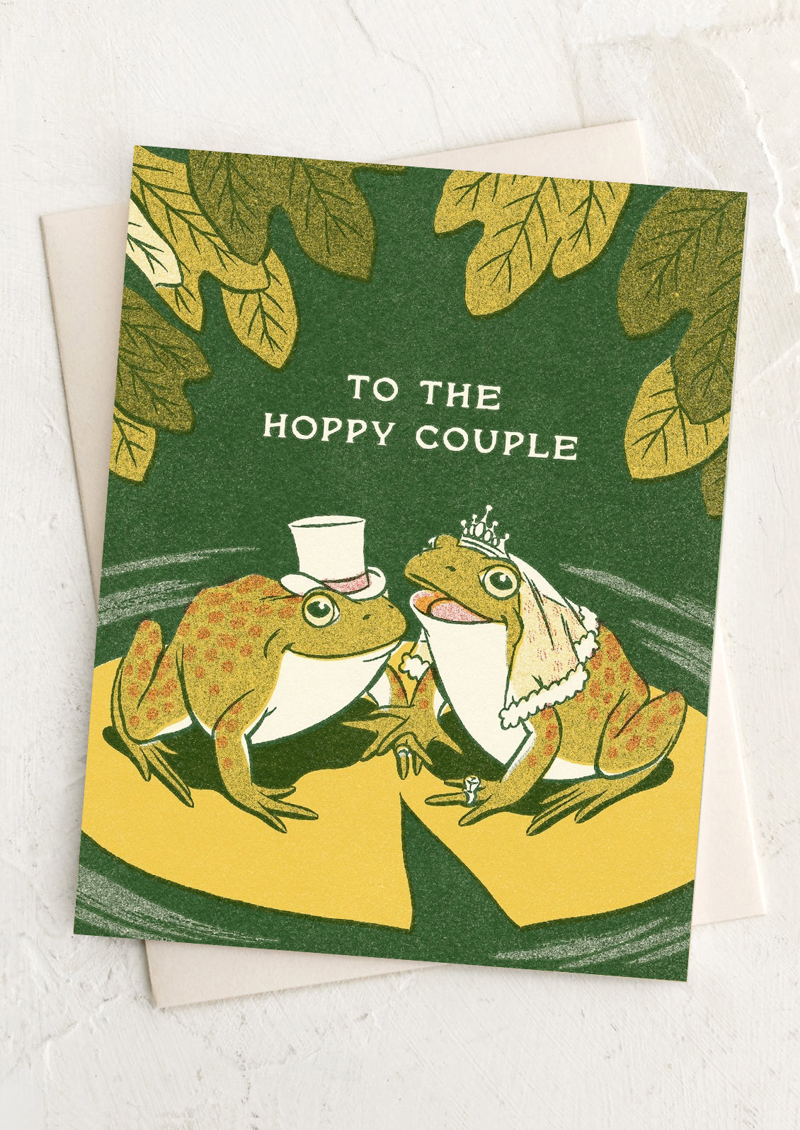 Greeting card with frogs in wedding attire and text 'To the Hoppy Couple' on a green background.