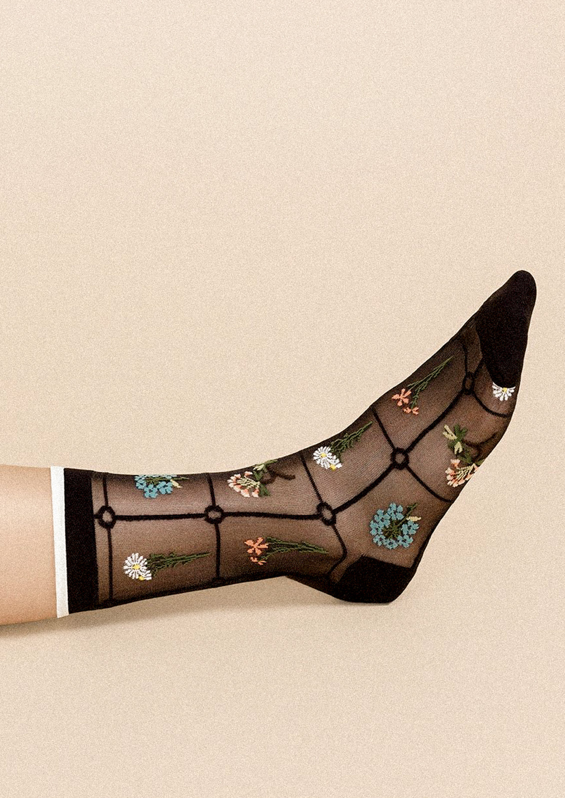 A person wearing a pair of semi-sheer black socks with various embroidered flowers.