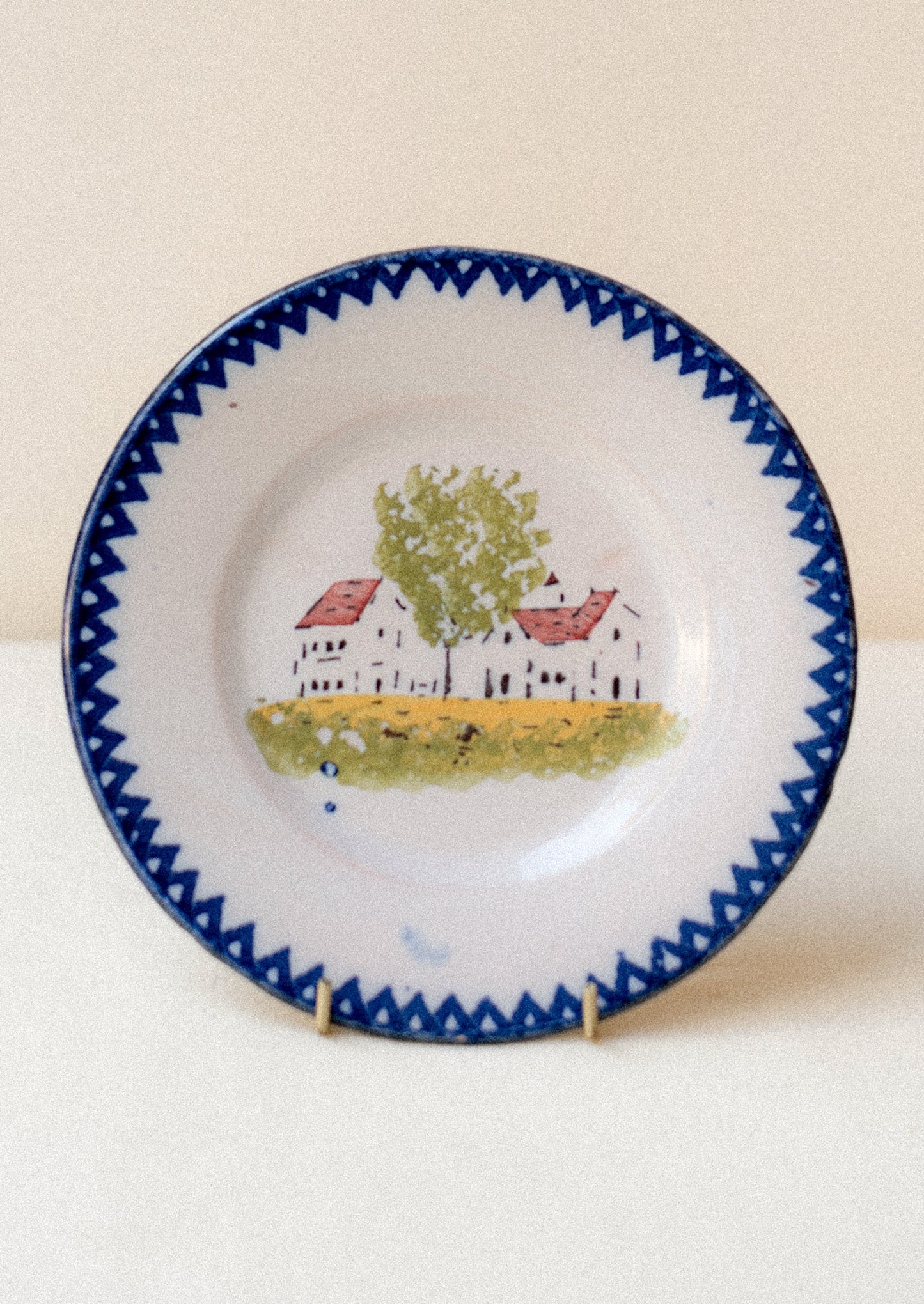 A plate with hand painted house motif and blue patterned rim.