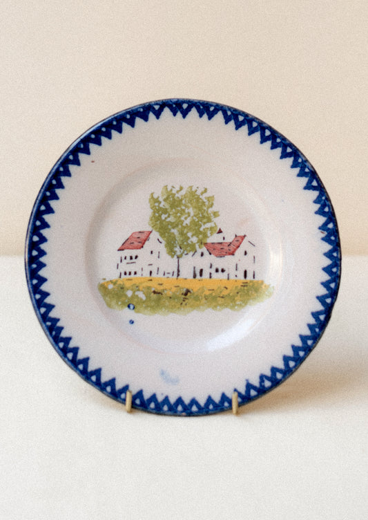 A plate with hand painted house motif and blue patterned rim.